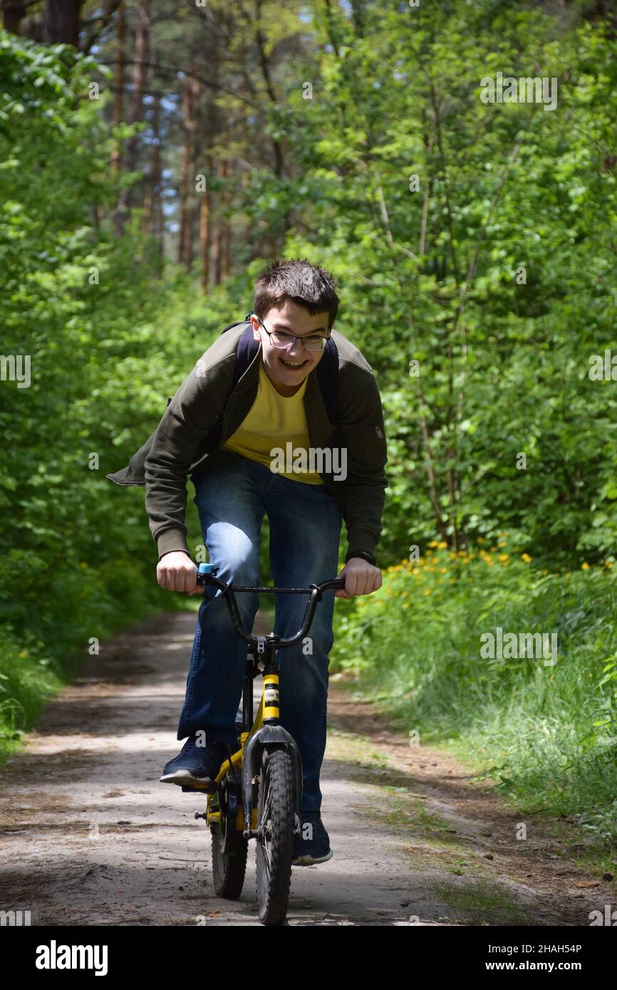 Un adolescente de unos 14 años que usa gafas es rápidamente montar una  bicicleta infantil a lo largo de un camino del bosque y reír. Vista frontal  Fotografía de stock - Alamy