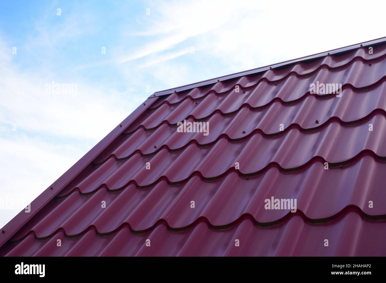 Parte de un techo de metal corrugado rojo contra un cielo azul. Hay un espacio vacío a la izquierda para insertar una etiqueta Foto de stock