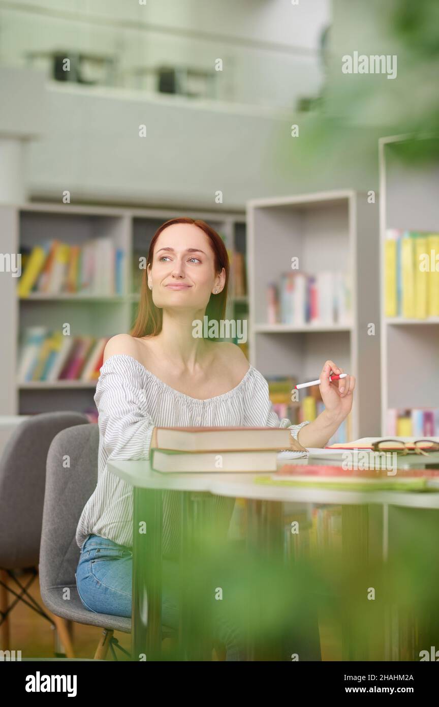 Mujer escribiendo en la mesa mirando penosamente a un lado Foto de stock