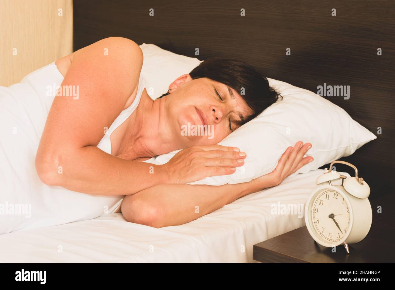Mujer de mediana edad dormida en la cama despertador en la mesita