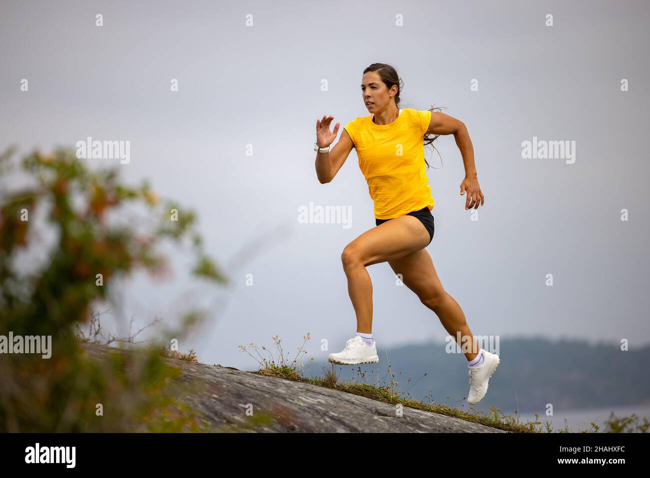 Mujer de fitness enfocada haciendo correr de alta intensidad en la ladera de la montaña mar Foto de stock
