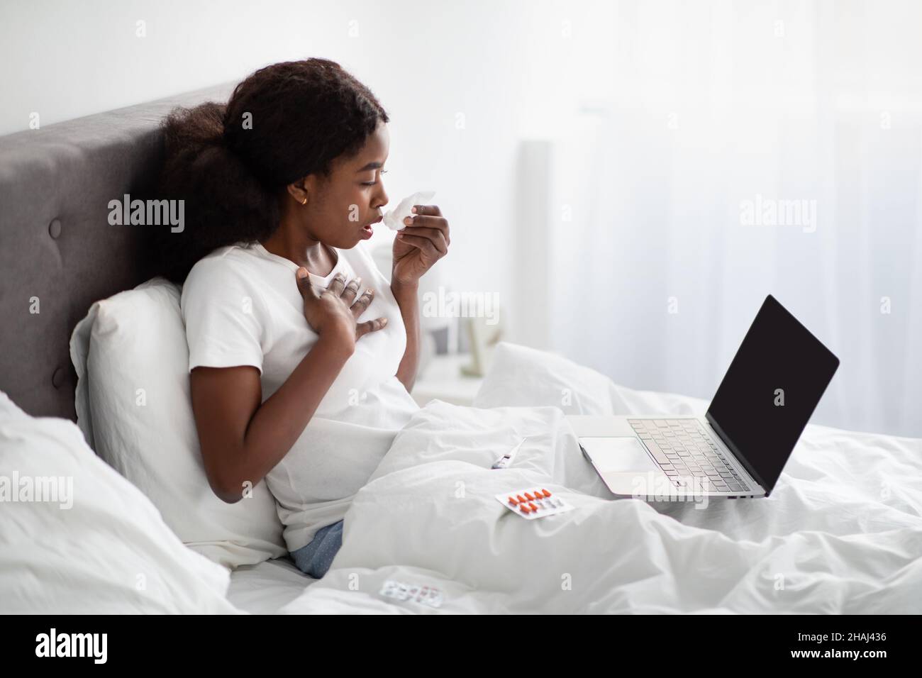 Mujer negra enferma tocando su pecho y usig portátil, se burla Foto de stock