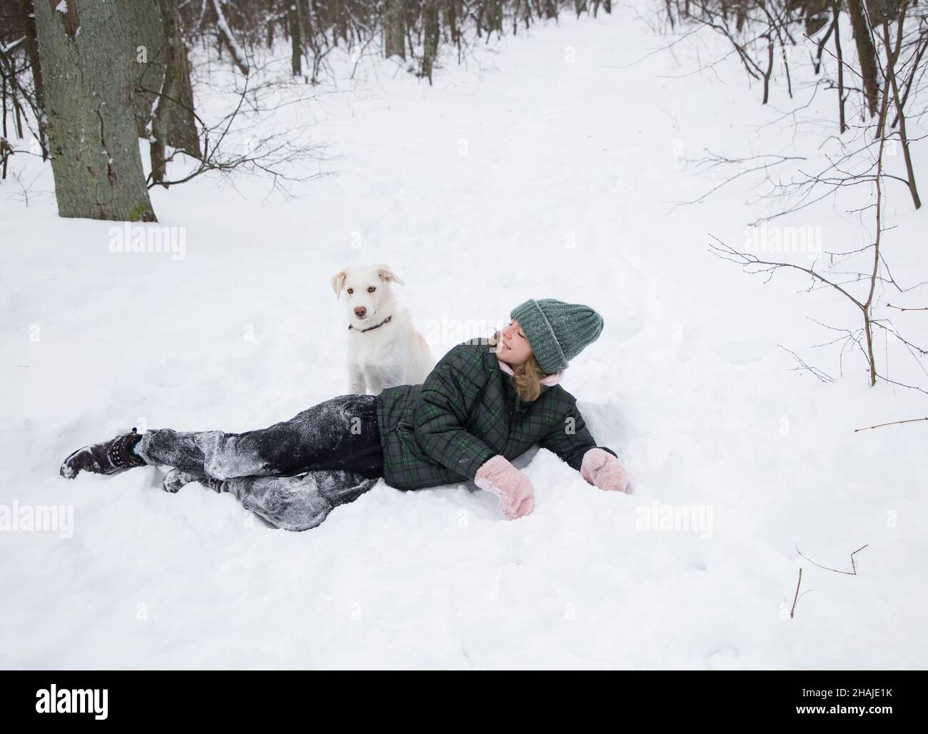 una adolescente de 16-17 años se encuentra en la nieve con un perro blanco. camine con su mascota en la temporada fría de invierno. Diversión con el querido perro. Un estilo de vida activo, alegría siempre Foto de stock