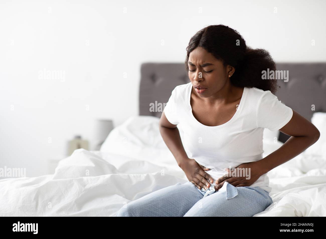 Mujer negra joven que sufre de dolor abdominal por la mañana Foto de stock