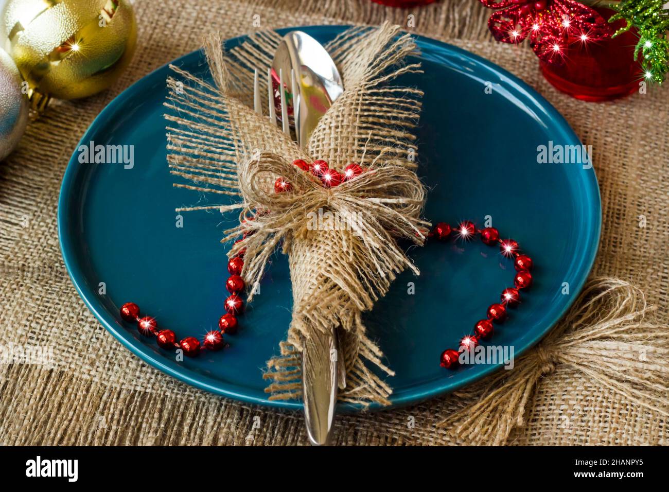 Cubertería con estilo envuelta en servilleta yute sobre plato de color azul  sobre superficie de burlap con decoraciones navideñas Fotografía de stock -  Alamy