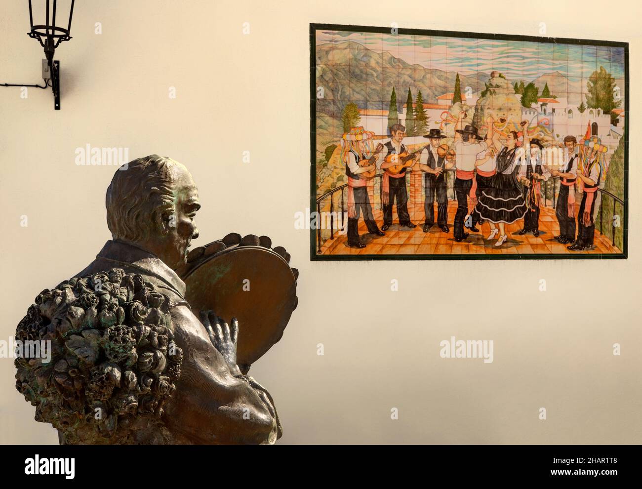 La escultura Al Fiesterero dedicada a las fiestas y un panel de cerámica cercano que relata la historia del pueblo de Comares, un pueblo de 703 metros de altura Foto de stock