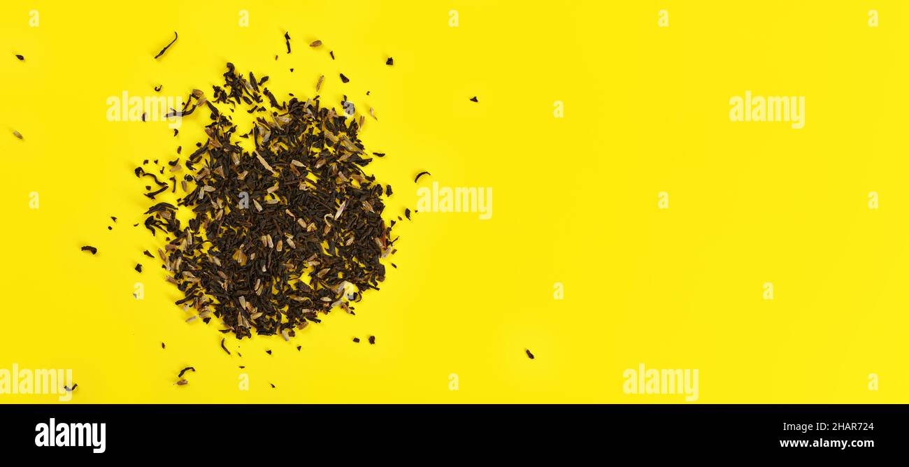 Té negro suelto con pocas flores secas en el tablero amarillo, vista desde arriba del espacio para texto lado derecho Foto de stock