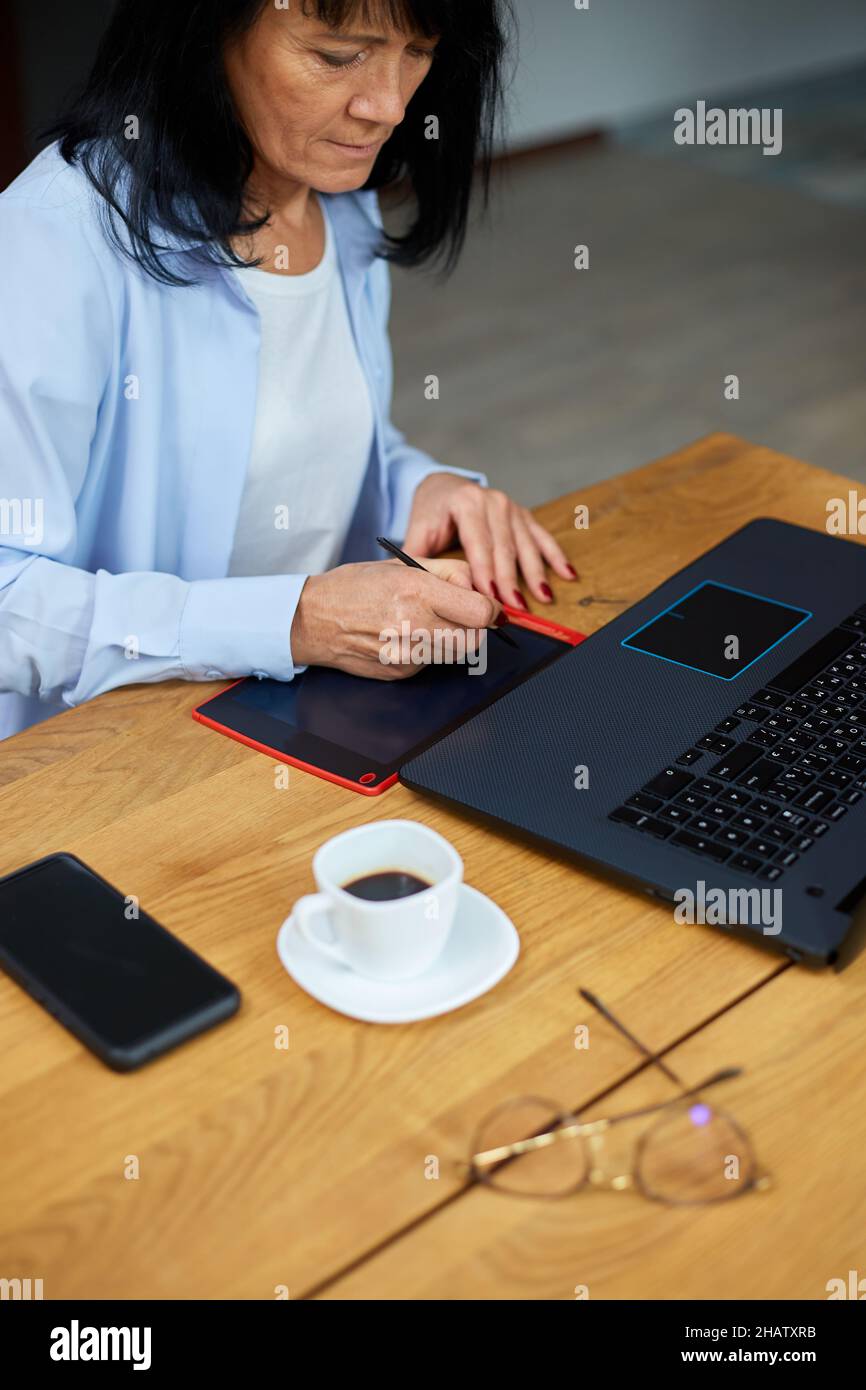 Diseñadora senior con tableta gráfica y lápiz óptico, trabajando en un  portátil, utilizando un ordenador y un digitalizador en una oficina  creativa Fotografía de stock - Alamy