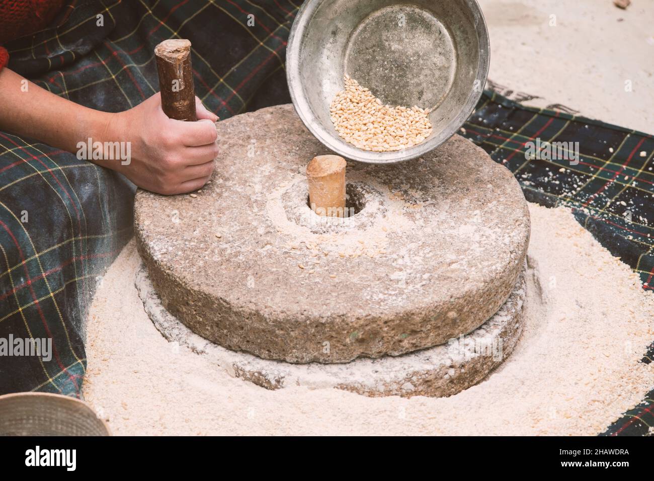 El antiguo molino de mano o piedra de la harina, muele el grano en harina.  Piedras de molienda hechas a mano antiguas. La anciana está moliendo harina  con lo tradicional Fotografía de