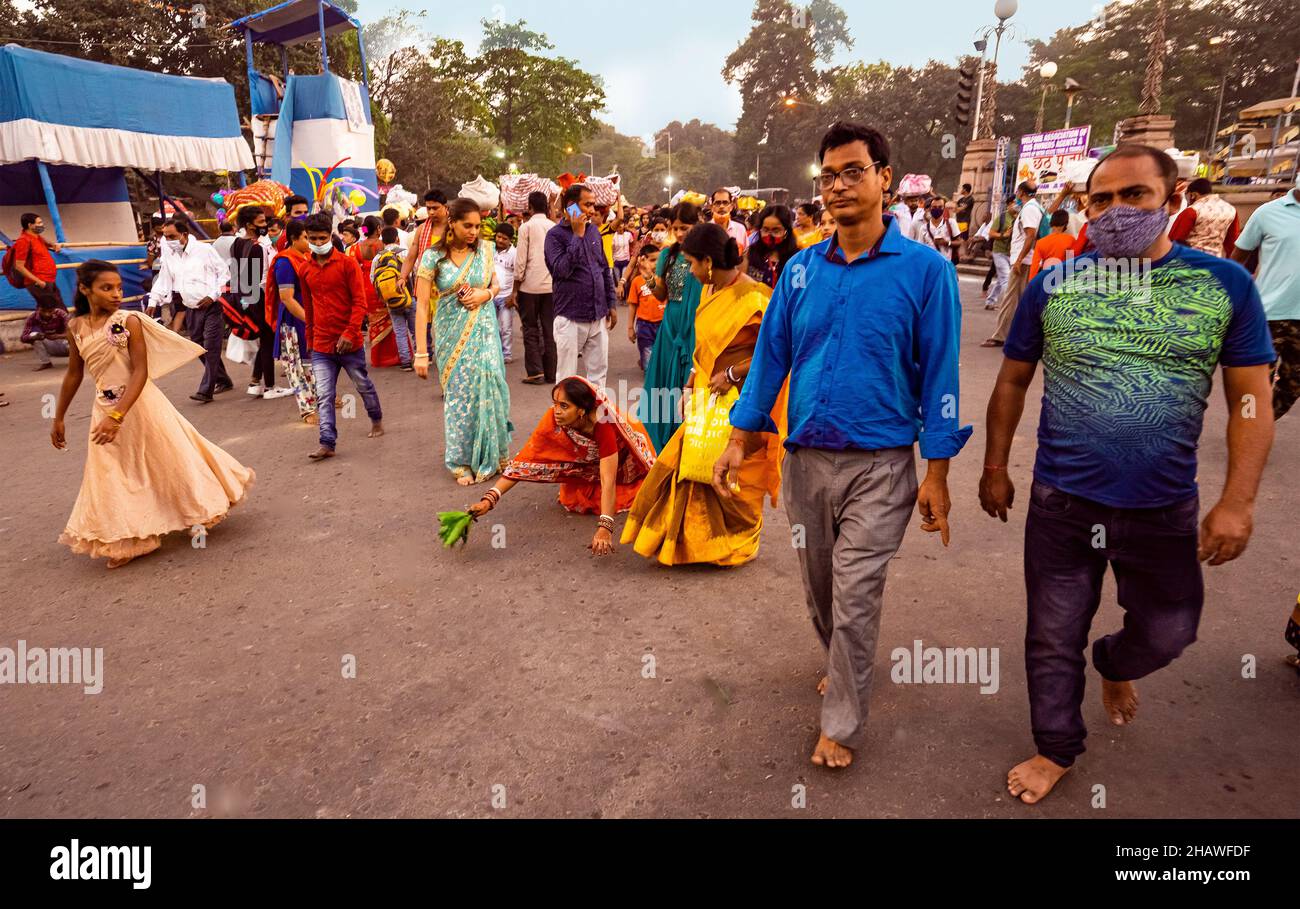 Mujer, peregrino, ( kneling down)En el camino a Eden Garden ghat, familia, visitantes, rápidamente en movimiento, al acercarse al anochecer,, Kolkata, India. Foto de stock