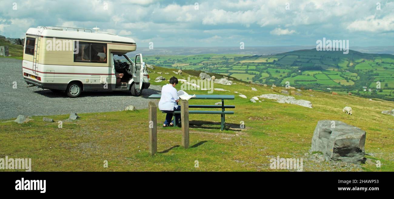 Brecon Beacons National Park Lay by VW RV Auto Sleeper Camper van mujer madura pasajero en la mesa de picnic vista de las colinas onduladas ovejas en el paisaje del Reino Unido Foto de stock