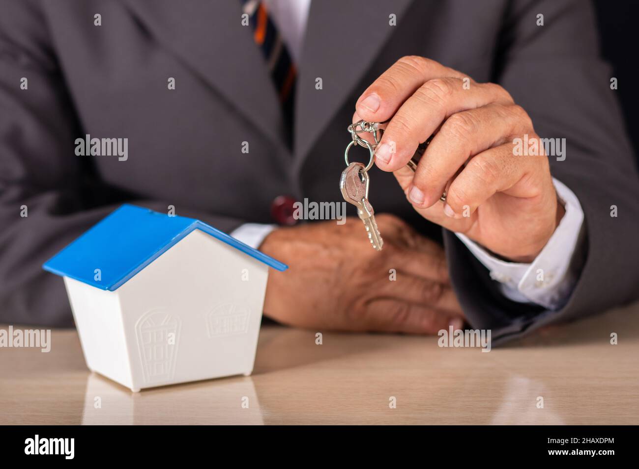 Hombre de negocios que sostiene la llave con la casa pequeña en la mesa. Concepto de vivienda. Foto de stock