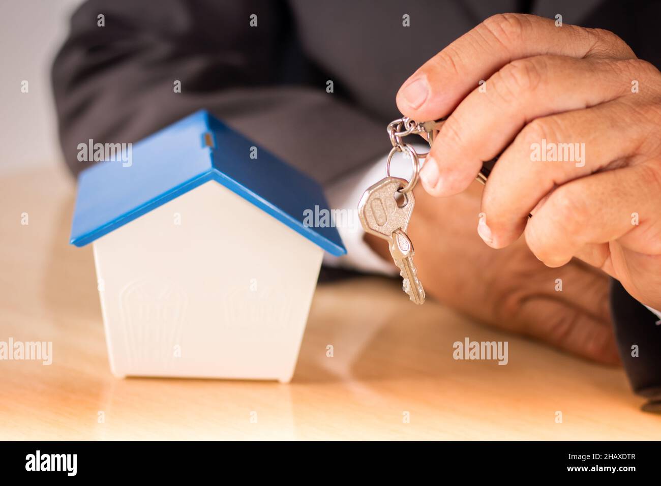 Hombre de negocios que sostiene la llave con la casa pequeña en la mesa. Concepto de vivienda. Foto de stock