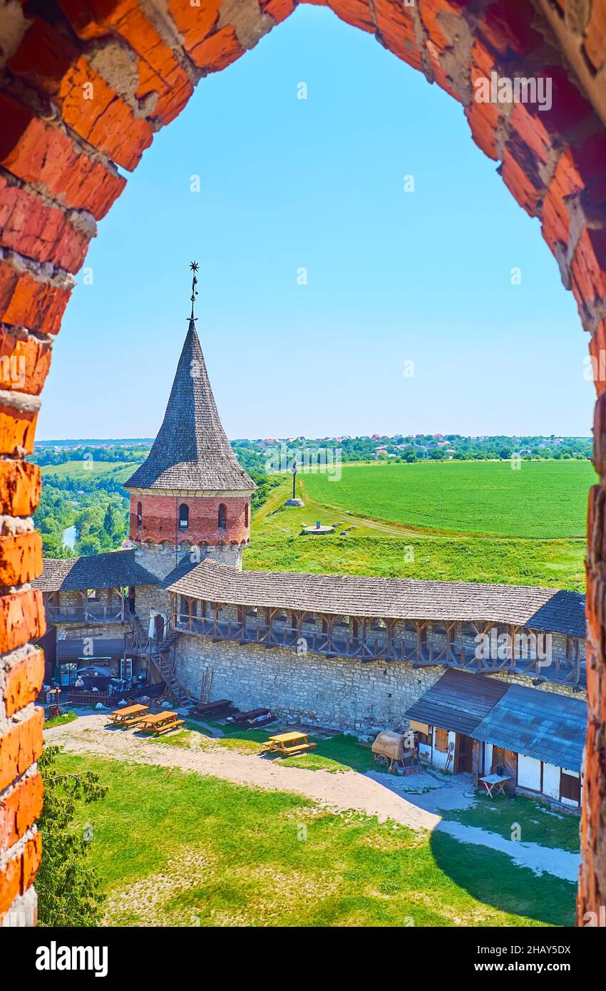La laguna de la antigua torre del Castillo de Kamianets-Podilskyi observa su patio, su ramera y su torre Laska con techo de cono contra el campo verde brillante Foto de stock