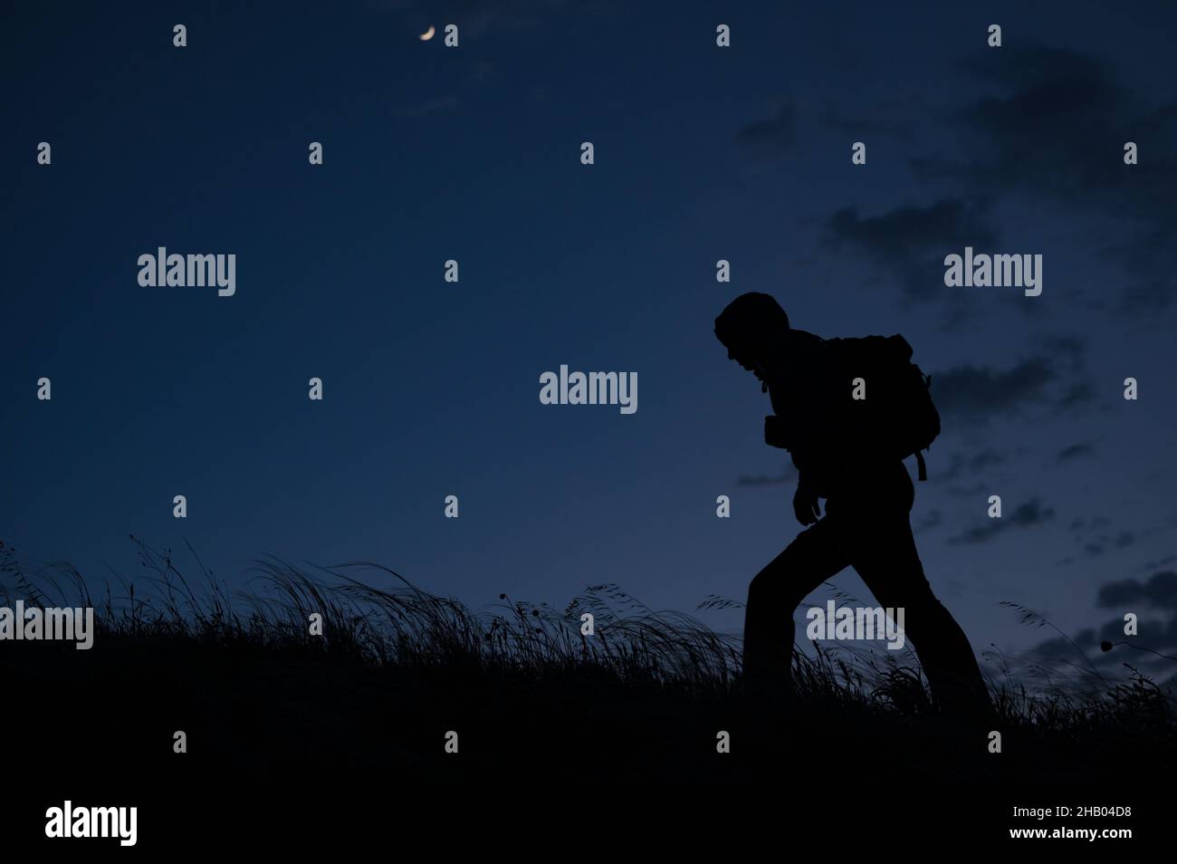 hombre solitario con mochila durante la noche al aire libre senderismo en colinas con viento soplante Foto de stock