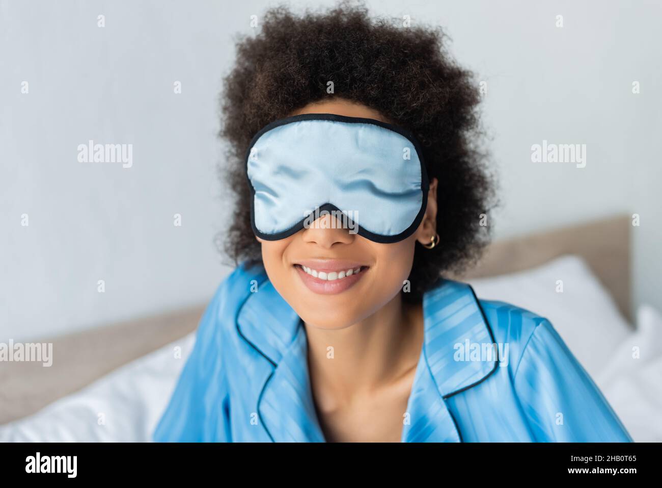 alegre mujer afroamericana en pijama azul y máscara de seda para dormir Foto de stock
