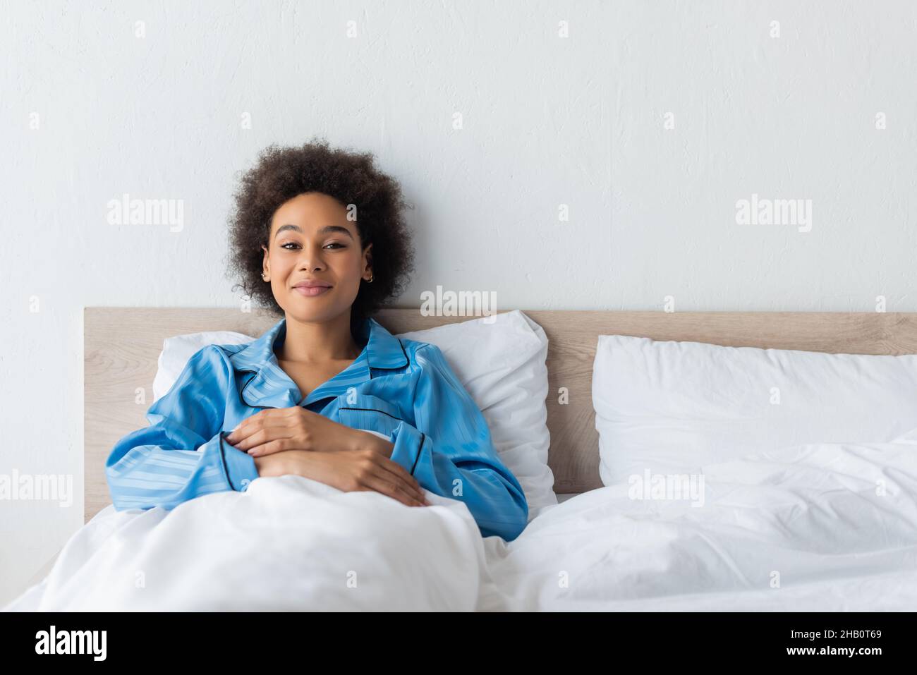 mujer afroamericana satisfecha en pijamas descansando en la cama Foto de stock