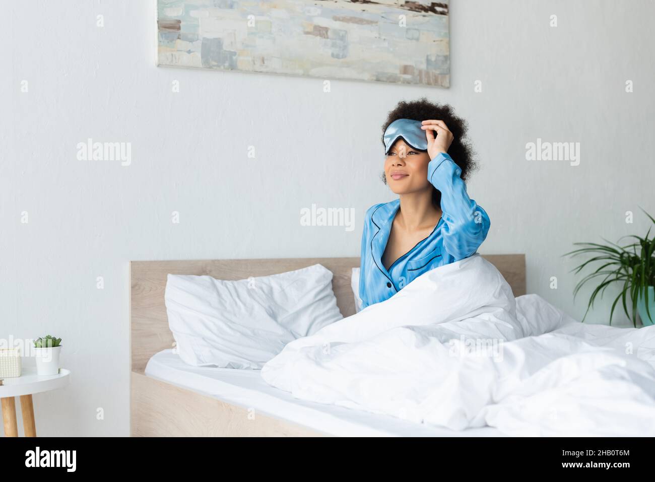 mujer afroamericana soñolienta en pijama que ajusta la máscara para dormir Foto de stock