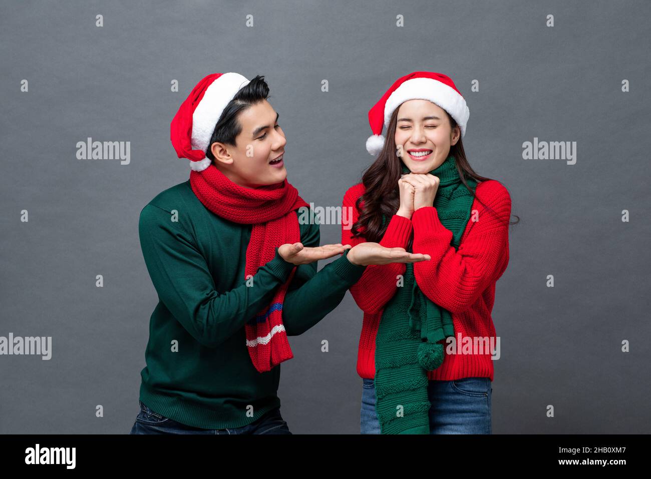 Joven hombre asiático guapo sorprendiendo a su novia en Navidad, estudio filmado en un fondo gris aislado Foto de stock