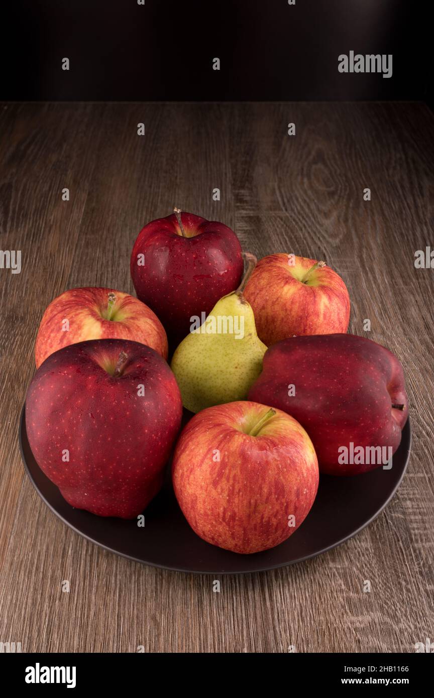 La foto muestra varias manzanas y una pera. La foto fue tomada en el estudio usando luz especial. La manzana roja brilla como brillante - esto es efecto natural. Foto de stock