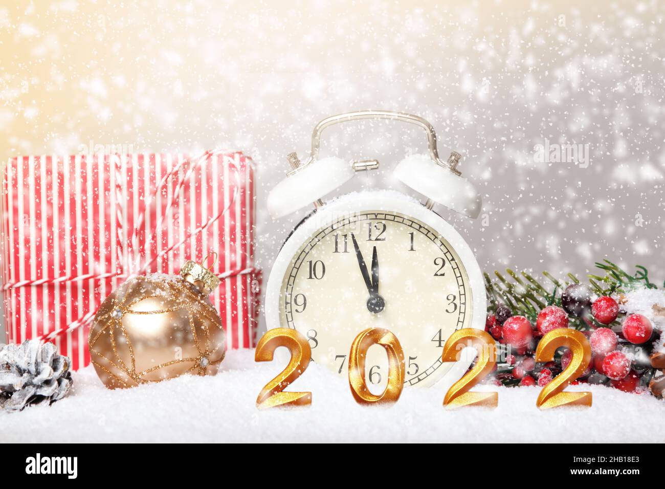 año nuevo 2022. Despertador con un regalo adornos navideños con una rama de abeto en la nieve. Foto de stock