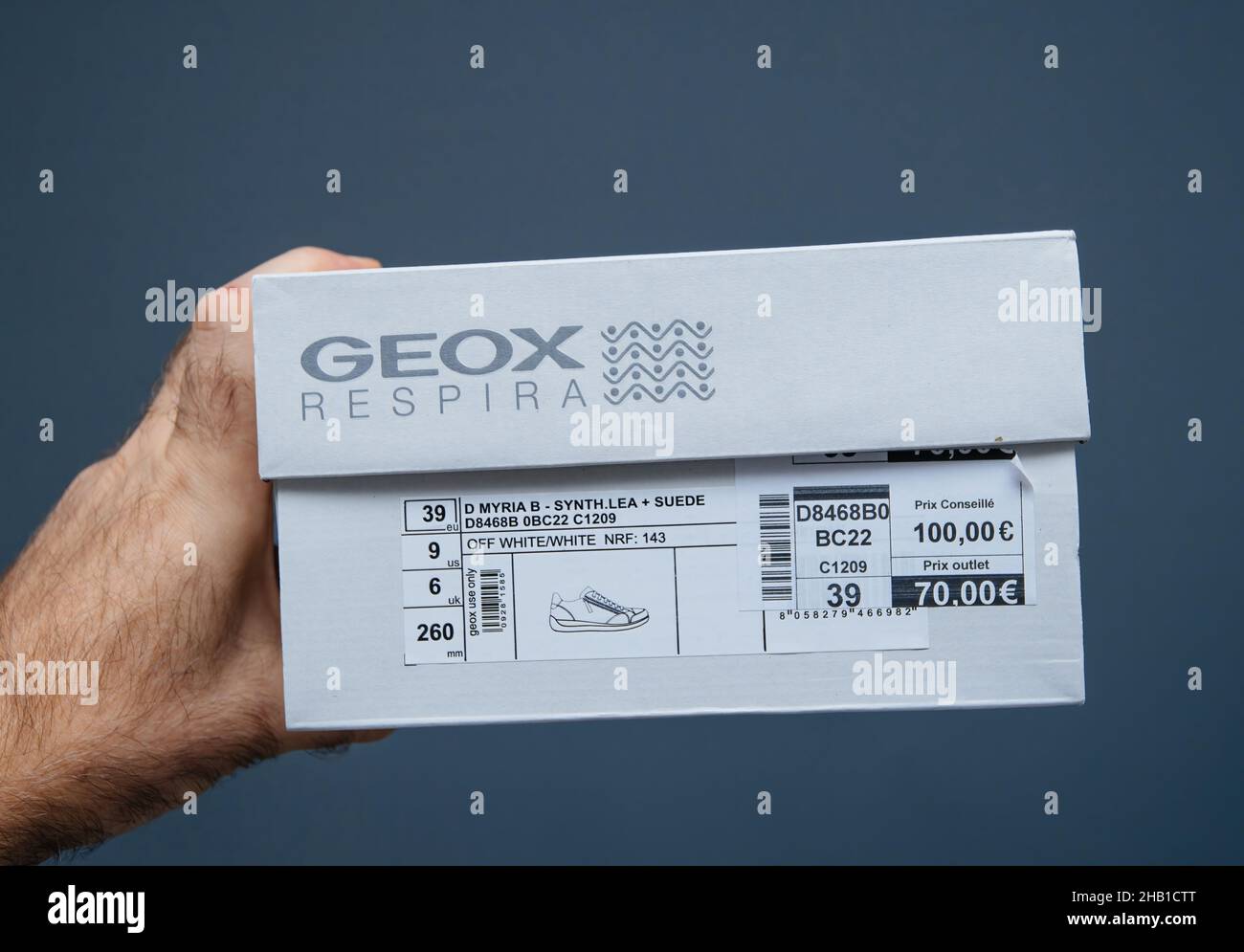 POV macho de mano con nuevos zapatos Geox Respira solated sobre fondo gris con el precio de 100 euros y descuento especial de salida de 70 euros Fotografía de -
