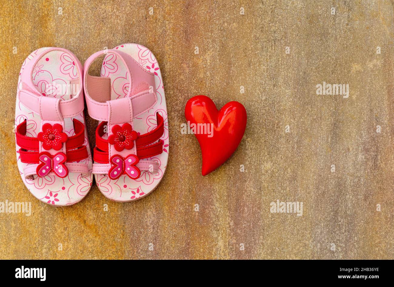 Flatlay con zapatos de sandalia para bebés y un corazón sobre fondo de madera con espacio de copia Foto de stock
