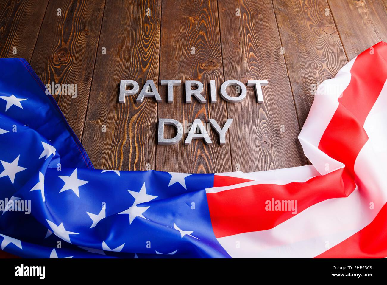 las palabras patriota día puso con letras de metal plateado en la superficie de la tabla de madera con la bandera ee.uu. arrugada Foto de stock