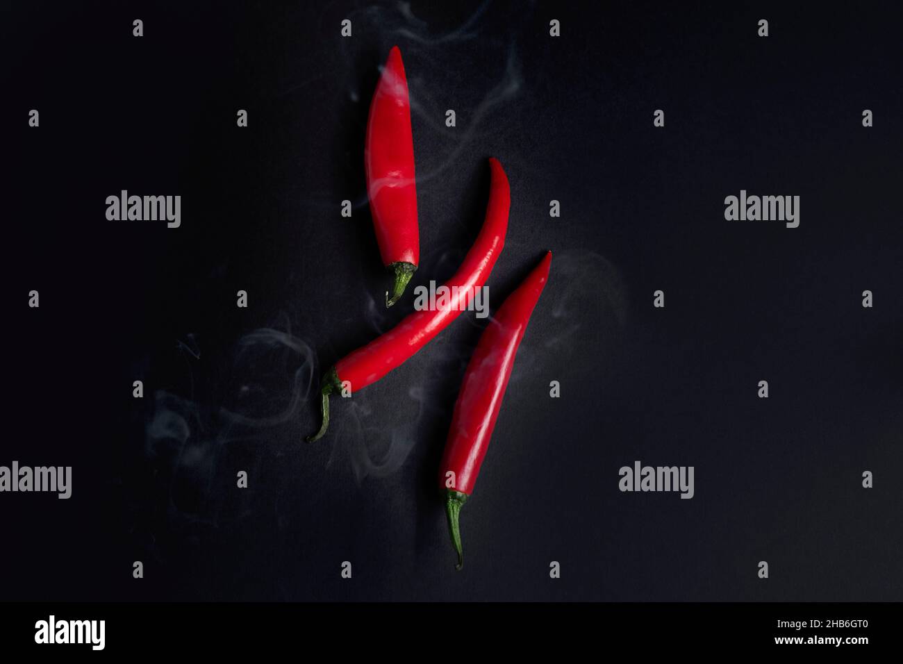 Pimientos rojos picantes calientes con humo proveniente de ellos sobre fondo negro oscuro, vista superior Foto de stock
