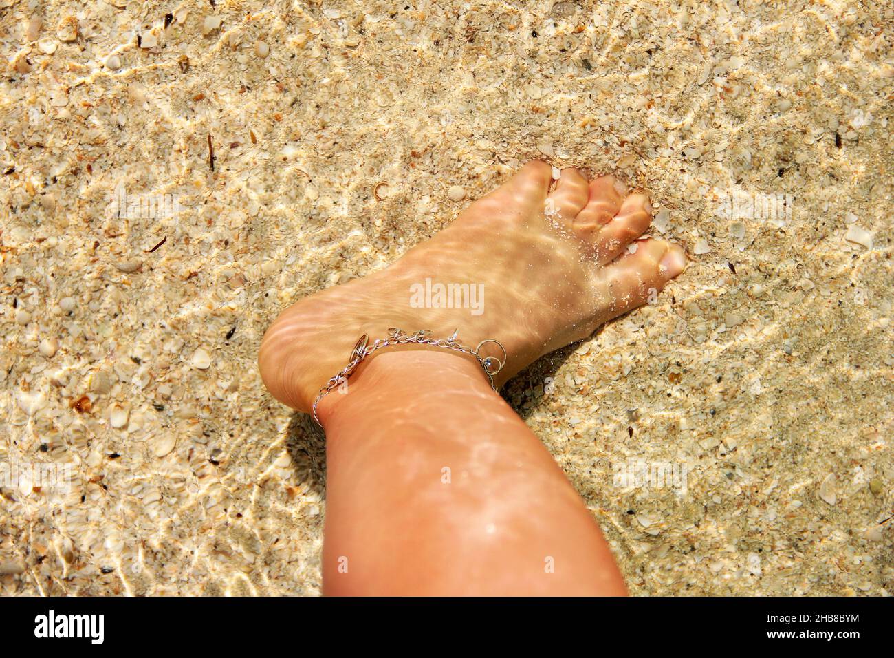 Hermoso pie femenino en el agua. Pulsera en el pie Foto de stock