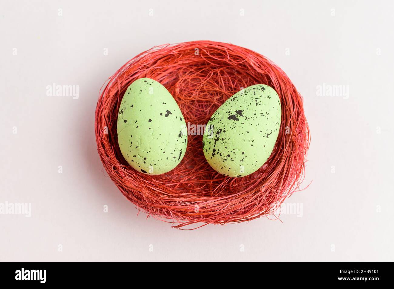 Dos huevos de Pascua decorativos de color verde en una cesta rústica roja aislada sobre una mesa blanca Foto de stock