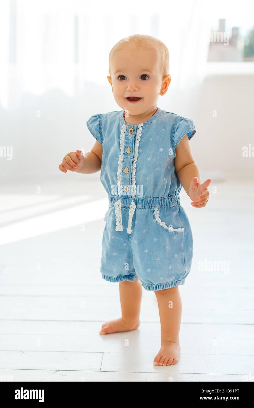 Lindo bebé sonriente niña de 1-2 años de edad llevar pantalones denim sport  y la parte superior blanca en la calle de la ciudad al aire libre. Mirando  la cámara. Infancia. Primavera