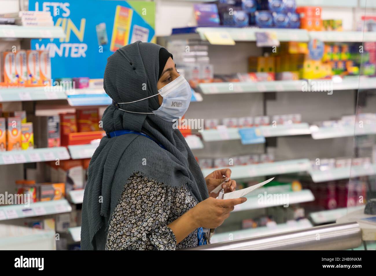 Mujer en Hijab y máscara de la cara con una receta en un mostrador de farmacia Londres Inglaterra Foto de stock