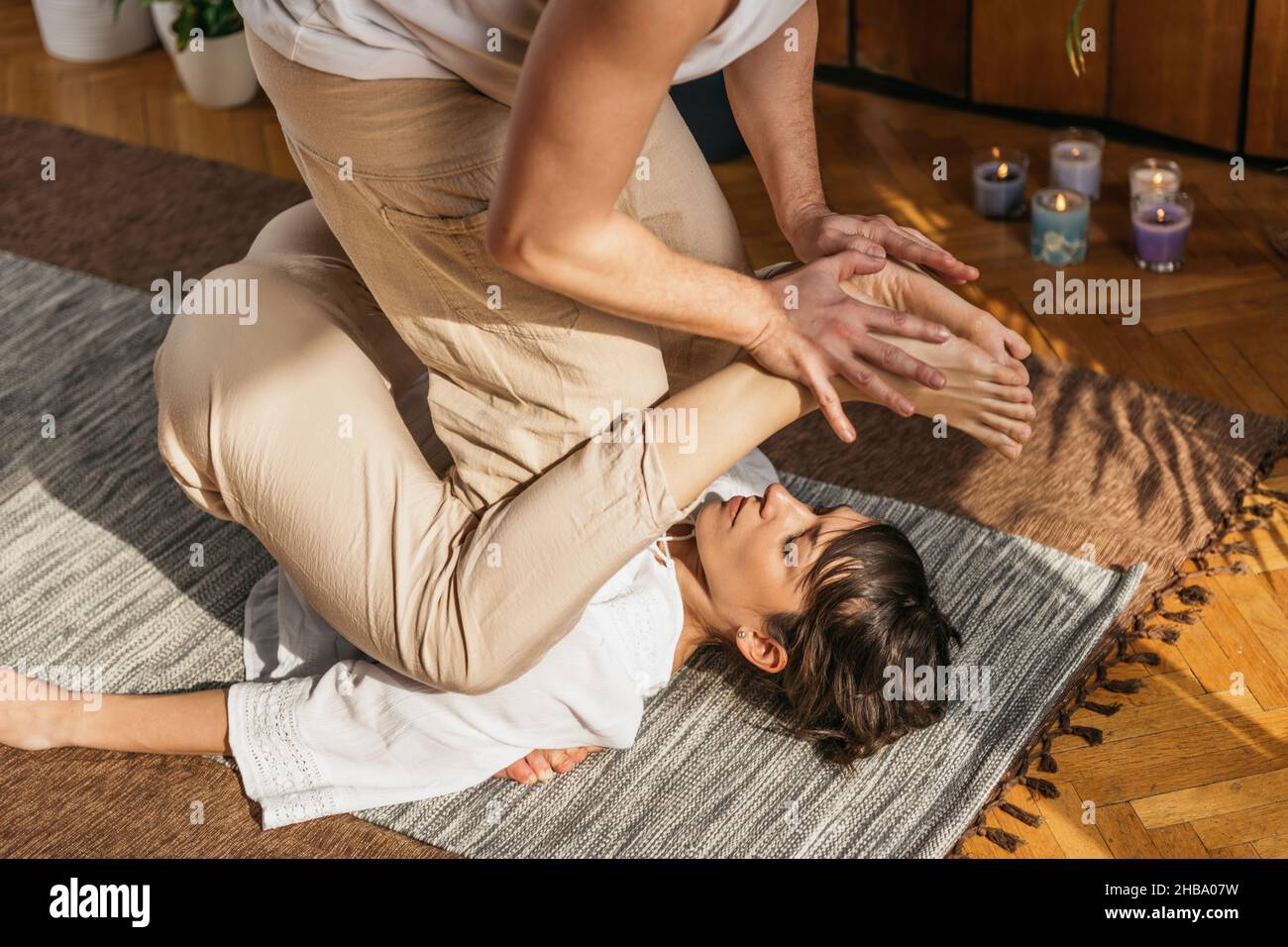 El practicante de masaje tailandés utiliza la postura de mariposa para estirar los tendones de la corva de una paciente femenina. Foto de stock