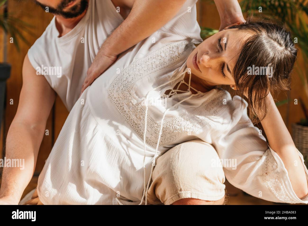 Masaje tailandés de estiramiento pasivo en la parte superior del cuerpo. Paciente femenino que recibe torsión espinal relajante. Postura de masaje tailandés que estira la espalda a cada lado del cuerpo. Foto de stock