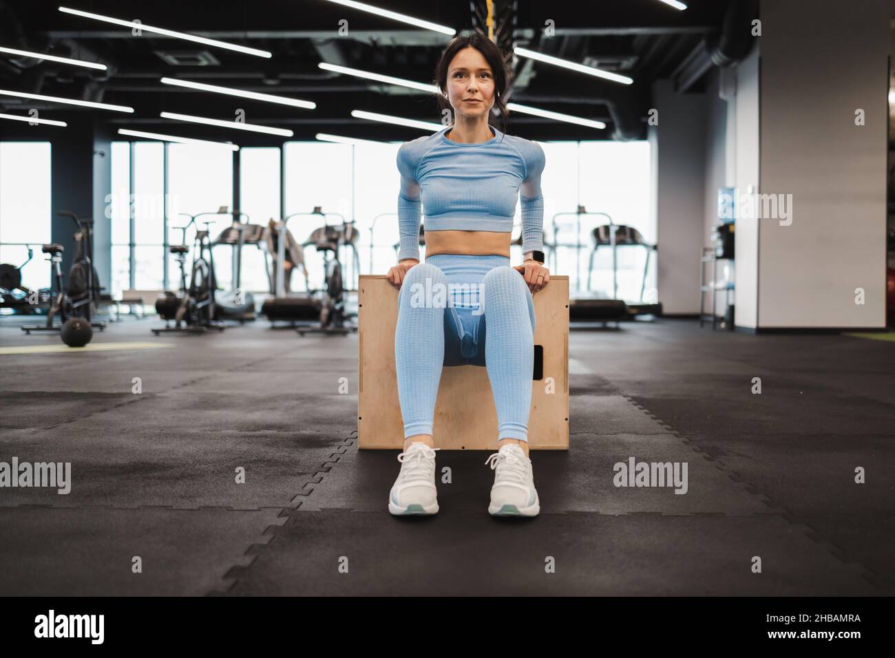 Mujer atlética en ropa deportiva azul haciendo ejercicios de tríceps en madera crossfit caja de salto en el gimnasio Foto de stock