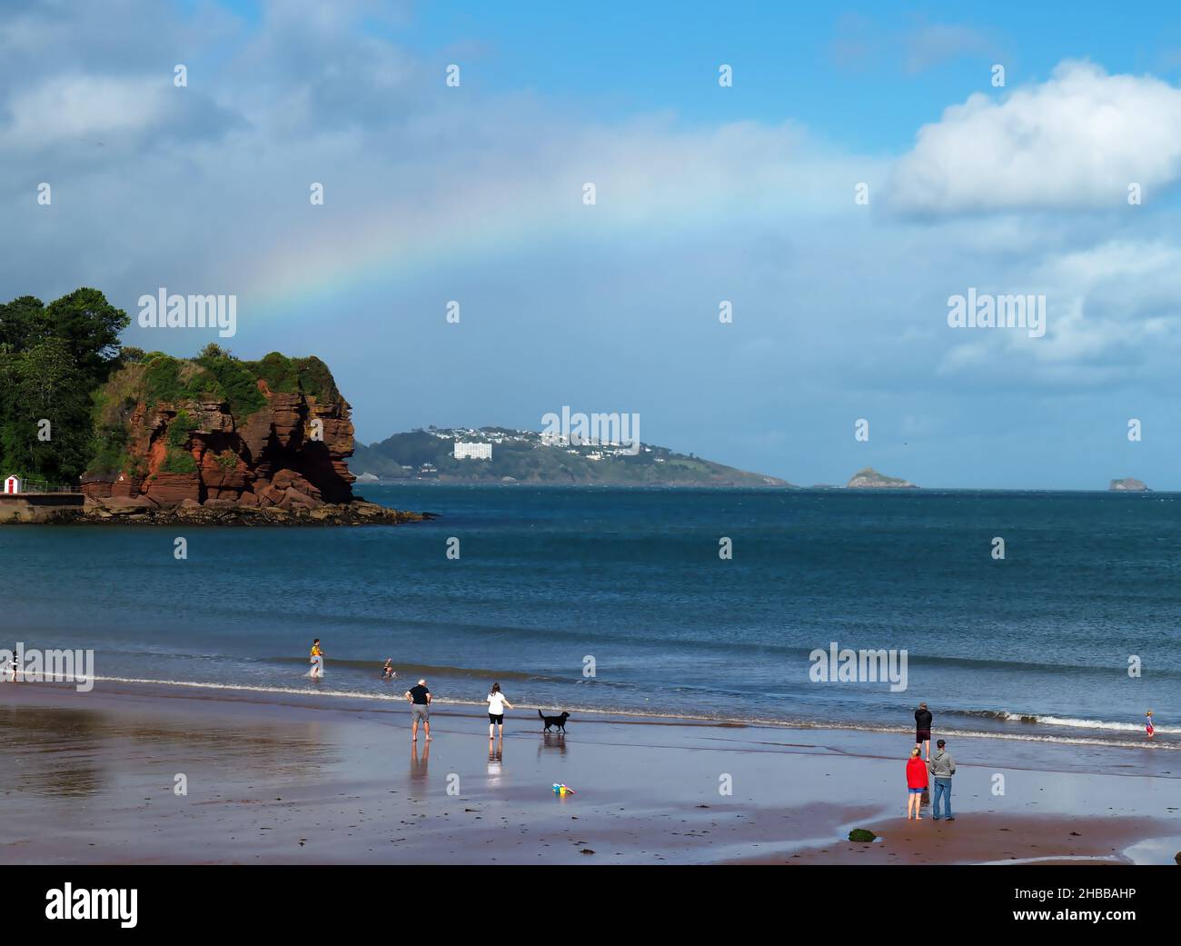Un arco iris sobre Tor Bay mientras la gente disfruta en la playa Goodrington Sands North, Paignton, Torbay, South Devon, Southwest England, Foto de stock