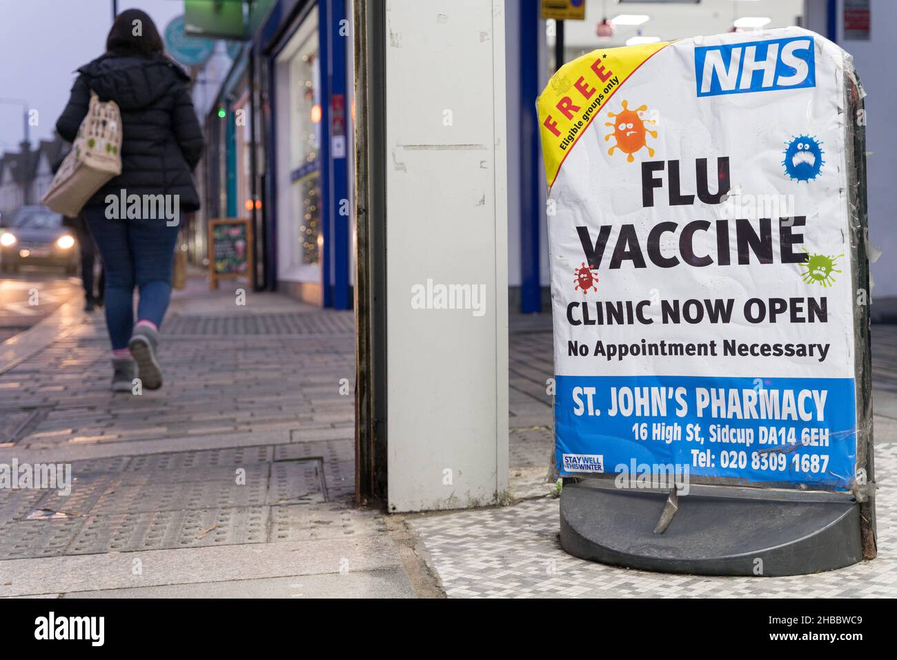 Los compradores de Navidad pasan el cartel de la vacuna contra la gripe que ofrece un puñetazo de gripe gratuito a las personas elegibles en la farmacia Sidcup de Londres Inglaterra Foto de stock