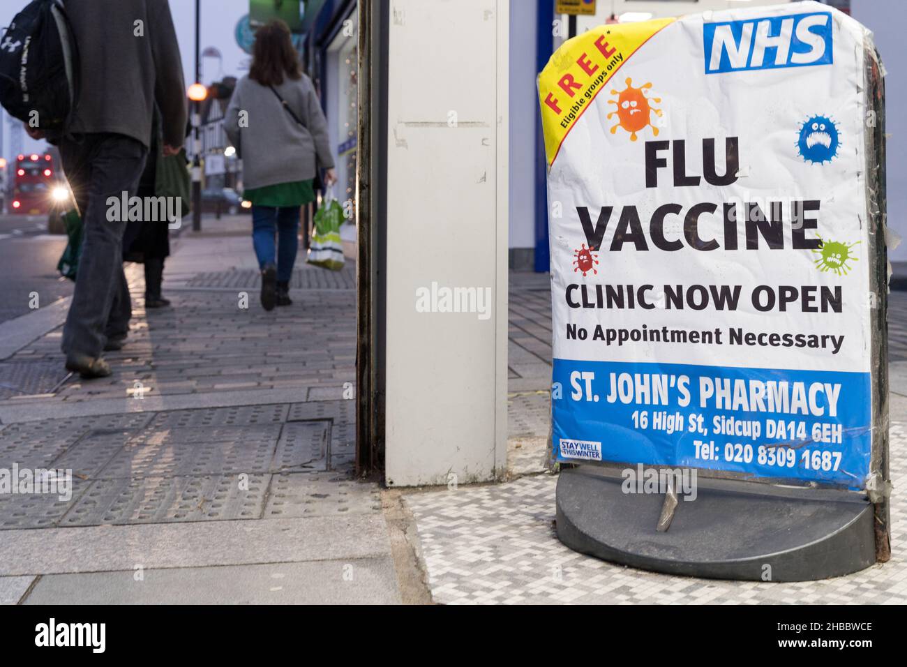 Los compradores de Navidad pasan el cartel de la vacuna contra la gripe que ofrece un puñetazo de gripe gratuito a las personas elegibles en la farmacia Sidcup de Londres Inglaterra Foto de stock