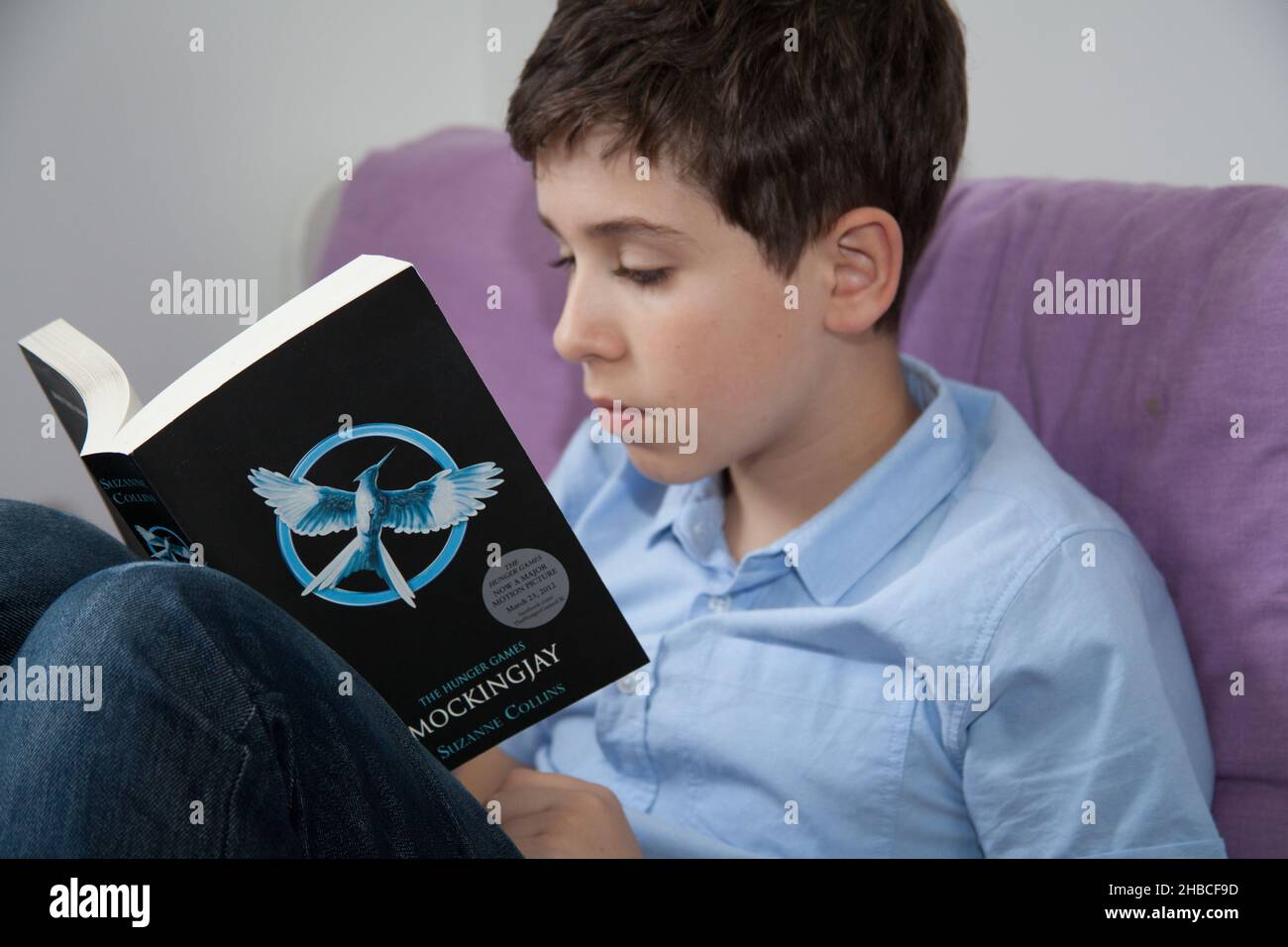 Un niño se sentó en una cómoda silla leyendo el Mockingjay de los juegos de Hambre de Suzanne Collins Foto de stock