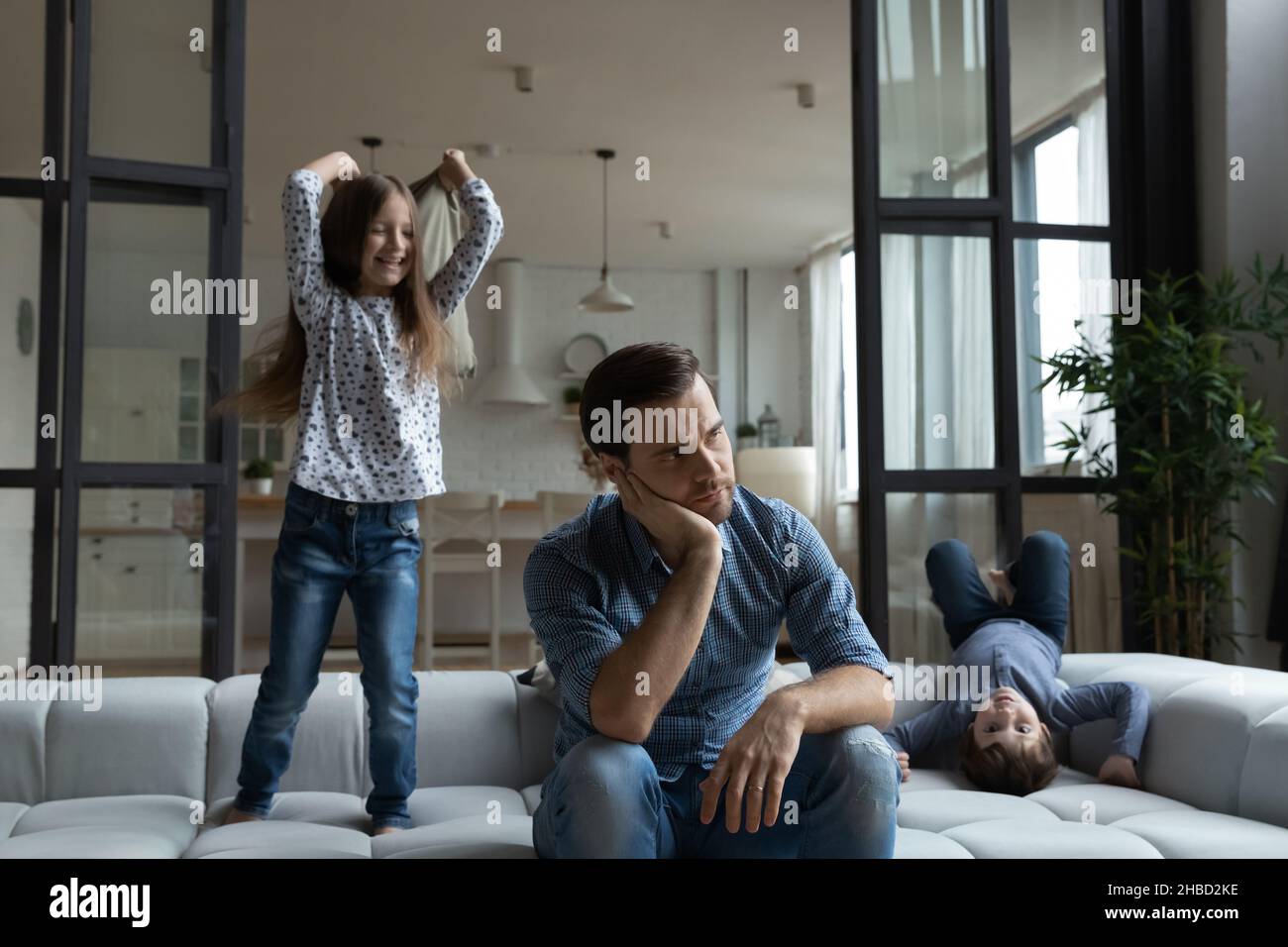 Padre cansado sentado en el sofá con hija e hijo ruidosos Foto de stock