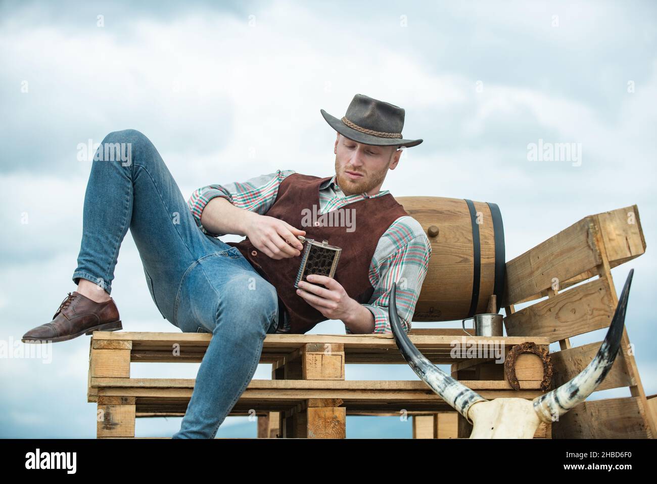 Hombre campesino vaquero en el lado del país con sombrero vaquero  occidental. Modelo masculino americano en el campo. Hombre atractivo con  whisky o brandy Fotografía de stock - Alamy