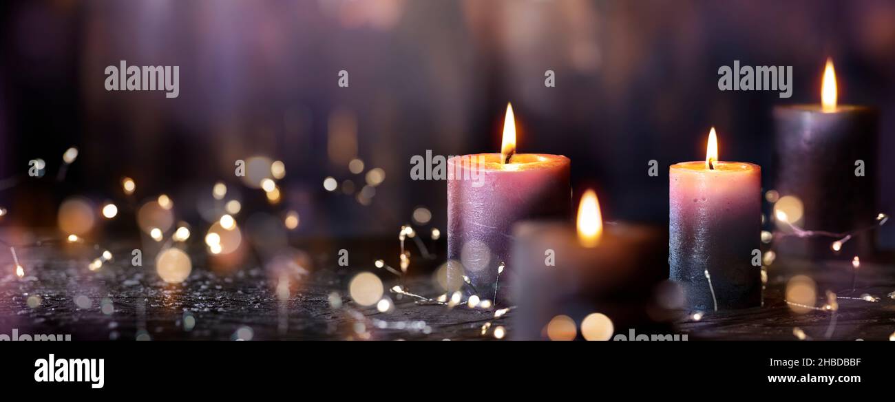 Velas Adviento - Cuatro velas votivas púrpura en la Iglesia con luces abstractas decocusadas Foto de stock