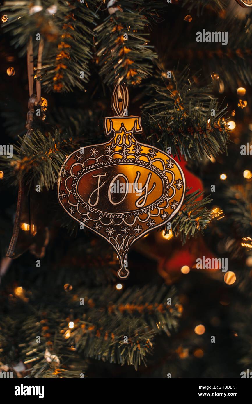 Juguete navideño dorado con ALEGRÍA de texto colgando en el árbol de Navidad. Luces doradas de verracas bokeh sobre fondo festivo de invierno Foto de stock