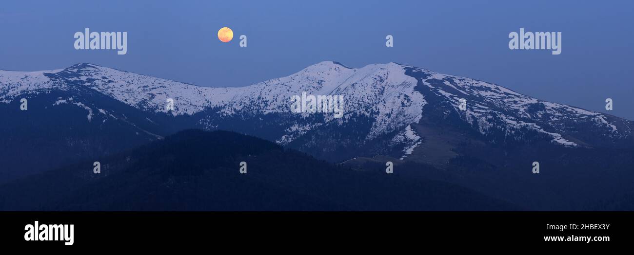 Paisaje primaveral con luna llena sobre una cresta. Crepúsculo por la mañana con un cielo claro. La última nieve en las cimas de las montañas. Cárpatos, Ucrania, Europa Foto de stock