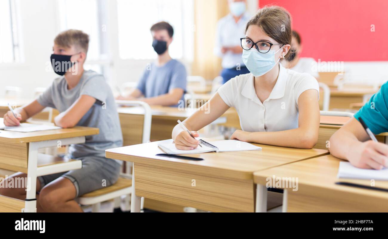 Adolescente en máscara protectora estudiando en la universidad con compañeros de clase Foto de stock
