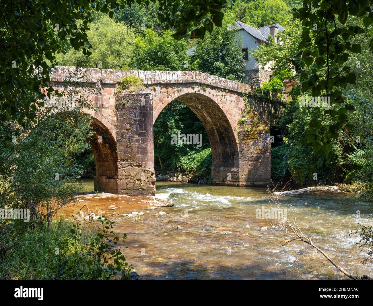 Puente romano de piedra de Conques en el camino de Santiago, cruzando un pequeño río tumultuoso, tomado en una mañana soleada de verano, sin gente Foto de stock