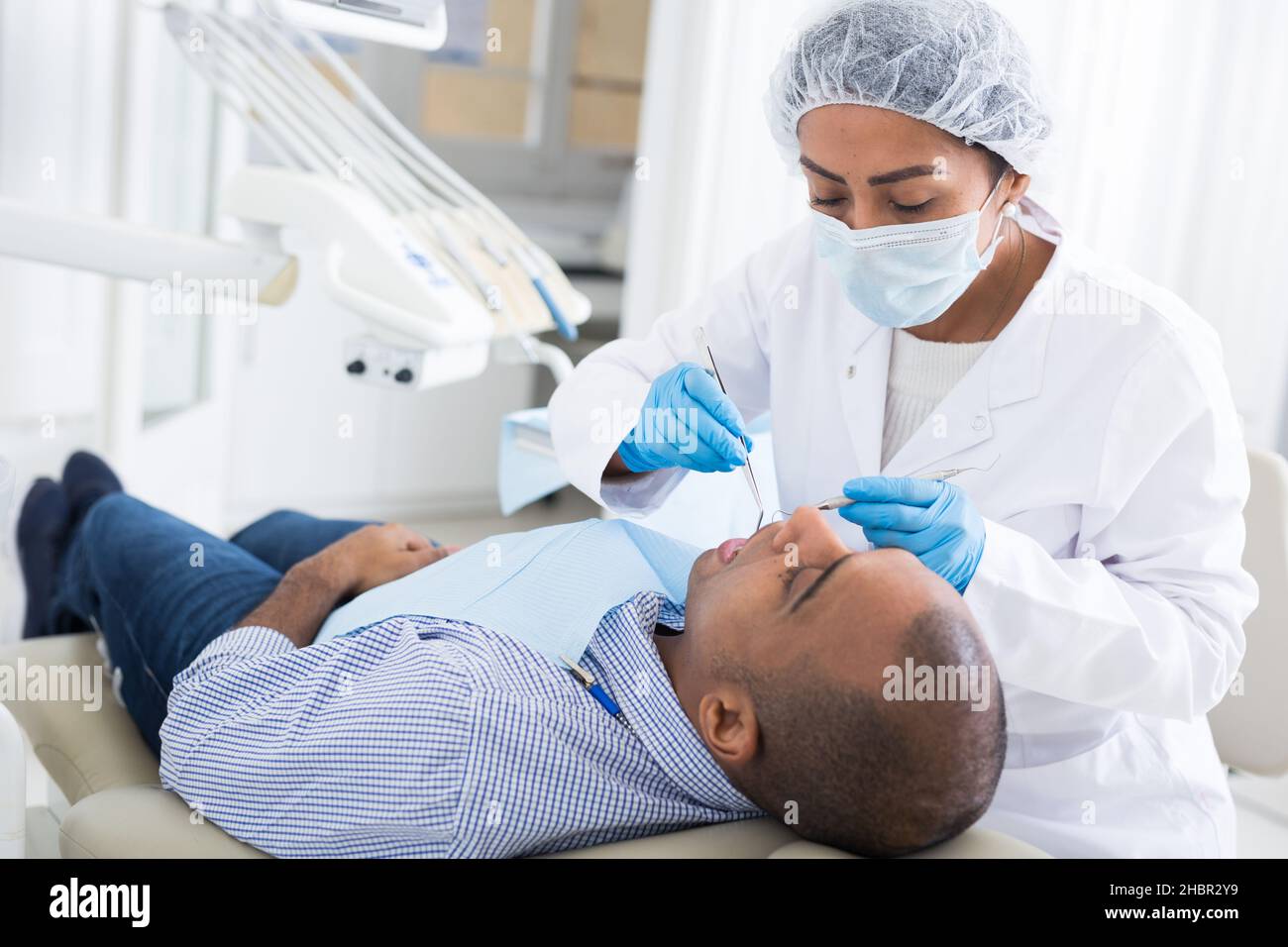 Dentista femenino hispano confiado que trata dientes de paciente