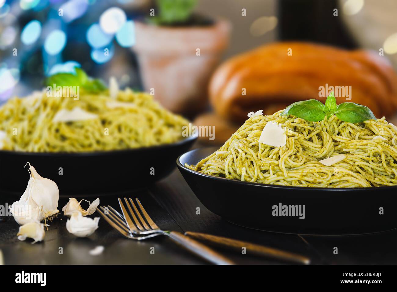 Enfoque selectivo de dos platos de pasta de pesto spaghetti con hojas frescas de albahaca y queso parmesano sobre una mesa de madera rústica negra. Foto de stock