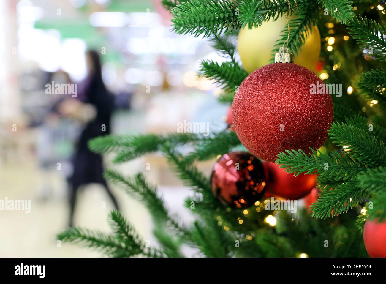 Venta de Navidad, árbol de Año Nuevo con bolas de juguete en un centro comercial en el fondo de la gente. Vacaciones de invierno y compras durante la pandemia de coronavirus Foto de stock